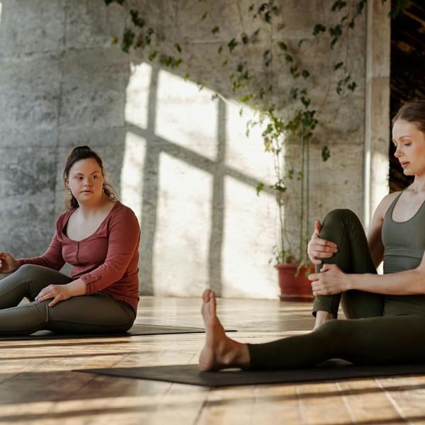 Person smiling and stretching gently on a yoga mat in a sunlit room.